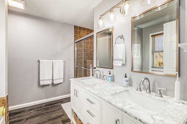 bathroom with tiled shower, wood finished floors, baseboards, and a sink