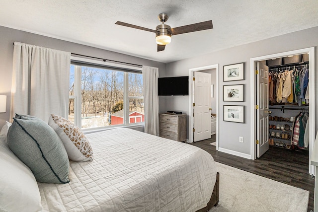 bedroom featuring a spacious closet, baseboards, dark wood finished floors, a closet, and a textured ceiling