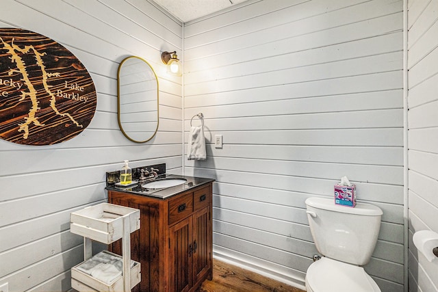 bathroom with toilet, wood finished floors, vanity, and wood walls