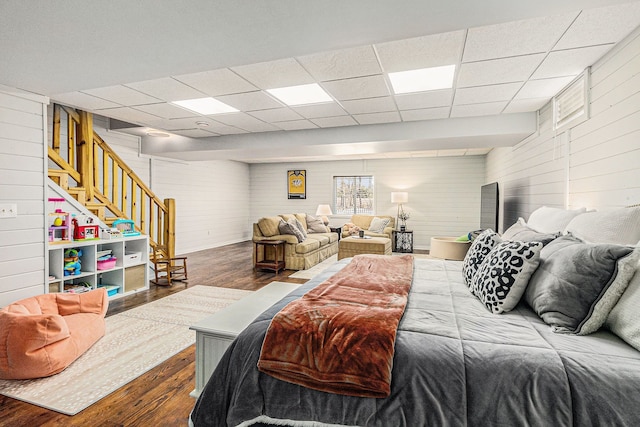 bedroom featuring a drop ceiling, wooden walls, and wood finished floors