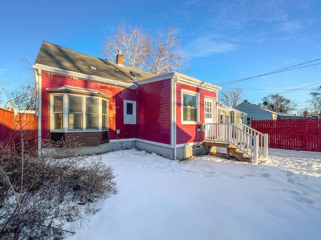 snow covered back of property with a chimney and fence