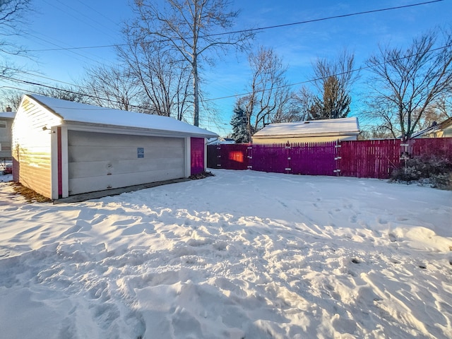 snow covered garage with a detached garage and fence