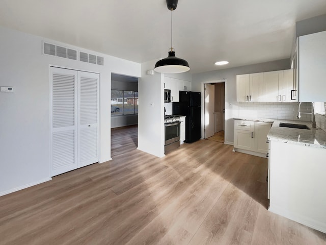 kitchen featuring visible vents, light wood-style flooring, a sink, backsplash, and stainless steel appliances