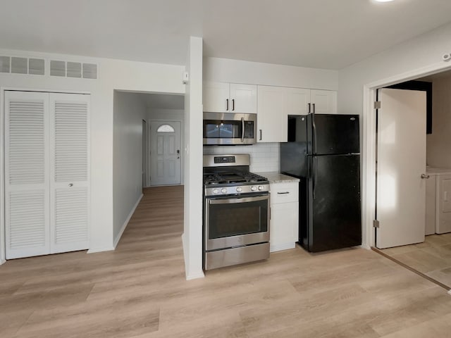 kitchen featuring light wood finished floors, washer / dryer, decorative backsplash, appliances with stainless steel finishes, and white cabinetry