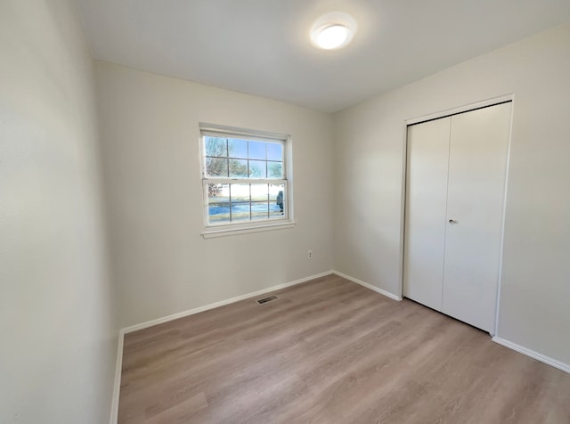 unfurnished bedroom featuring light wood-style flooring, baseboards, visible vents, and a closet