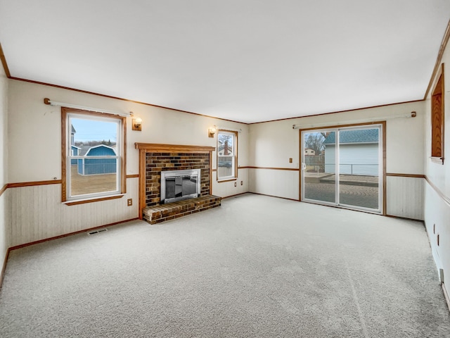 unfurnished living room featuring visible vents, ornamental molding, carpet floors, wainscoting, and a brick fireplace