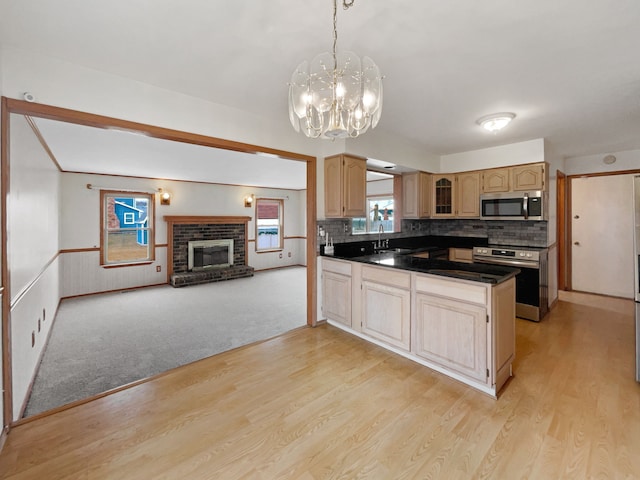 kitchen with a peninsula, a fireplace, light brown cabinetry, appliances with stainless steel finishes, and dark countertops