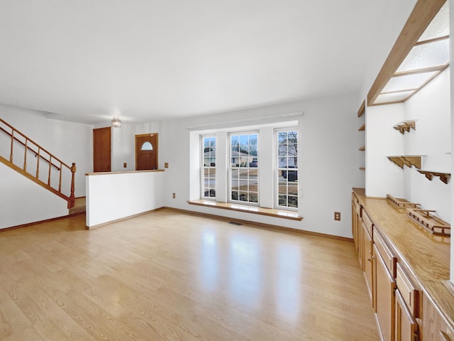 unfurnished living room featuring visible vents, stairway, light wood-style floors, and baseboards