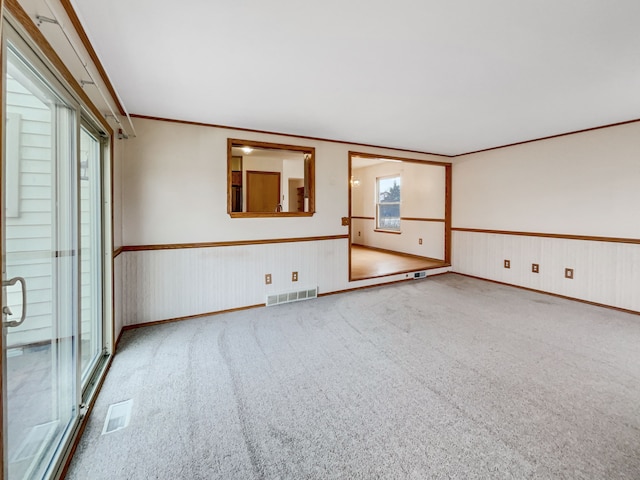 empty room with visible vents, wainscoting, crown molding, and carpet