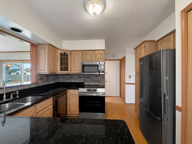 kitchen with a sink, backsplash, light wood-style floors, and appliances with stainless steel finishes