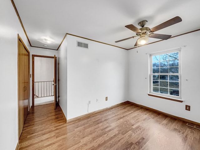 empty room featuring light wood-style floors, visible vents, and ornamental molding