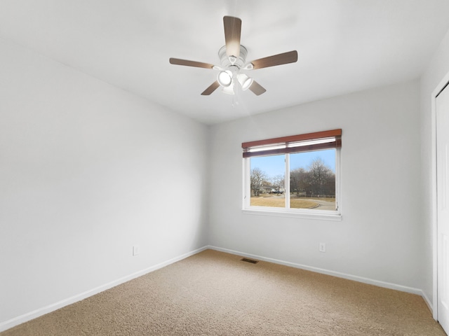 carpeted spare room with visible vents, baseboards, and ceiling fan