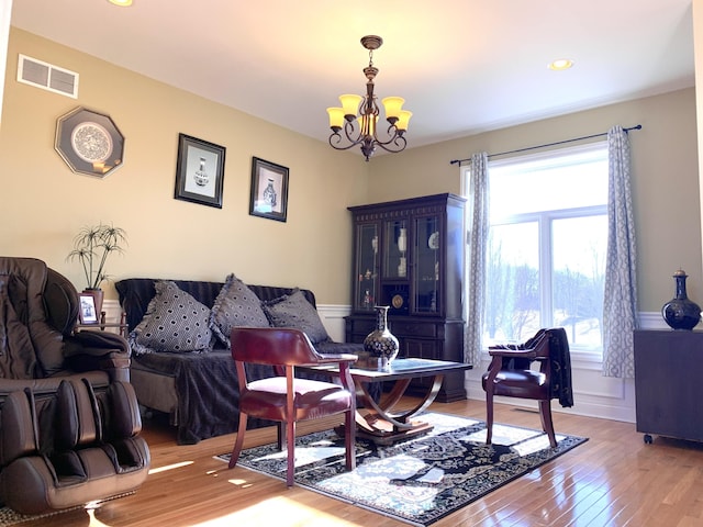 living area featuring visible vents, a wainscoted wall, light wood-style floors, an inviting chandelier, and a decorative wall