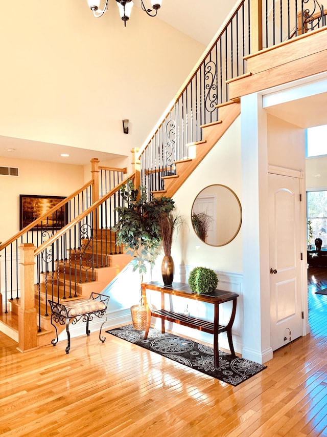 staircase with visible vents, baseboards, a towering ceiling, and hardwood / wood-style floors