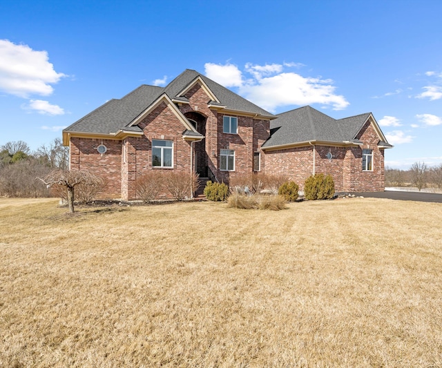 traditional-style house featuring brick siding, a front lawn, and a shingled roof