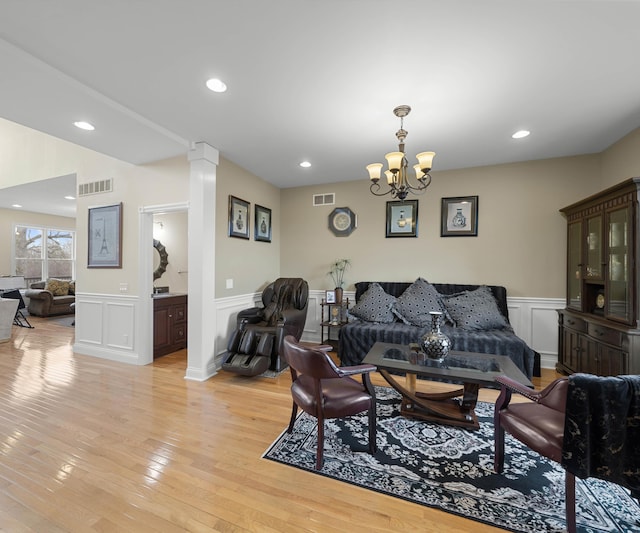 living room featuring light wood finished floors, visible vents, an inviting chandelier, and decorative columns