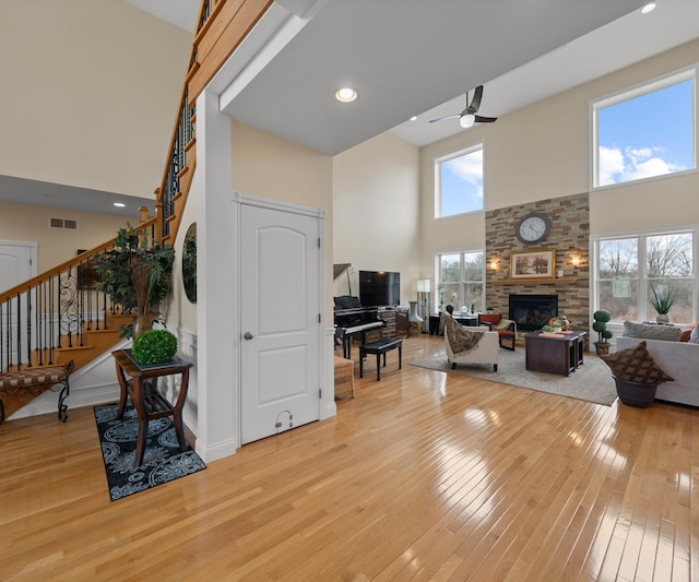 living area with visible vents, stairs, light wood-style flooring, a towering ceiling, and a glass covered fireplace