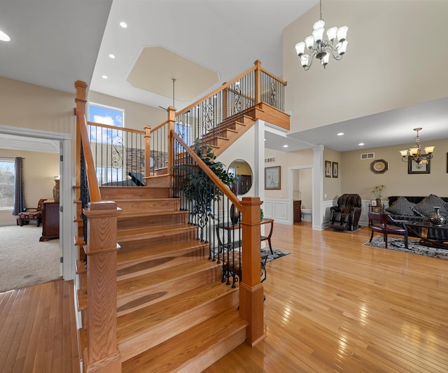 staircase featuring visible vents, an inviting chandelier, decorative columns, hardwood / wood-style flooring, and a towering ceiling