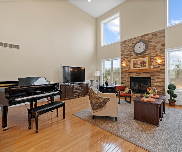 living room with light wood-type flooring, visible vents, a high ceiling, and a fireplace