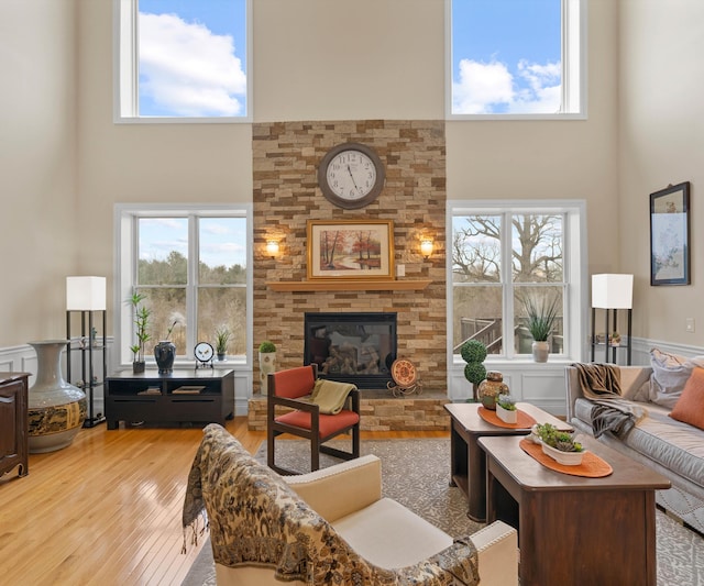 living room featuring a wainscoted wall, light wood-style floors, a towering ceiling, and a fireplace