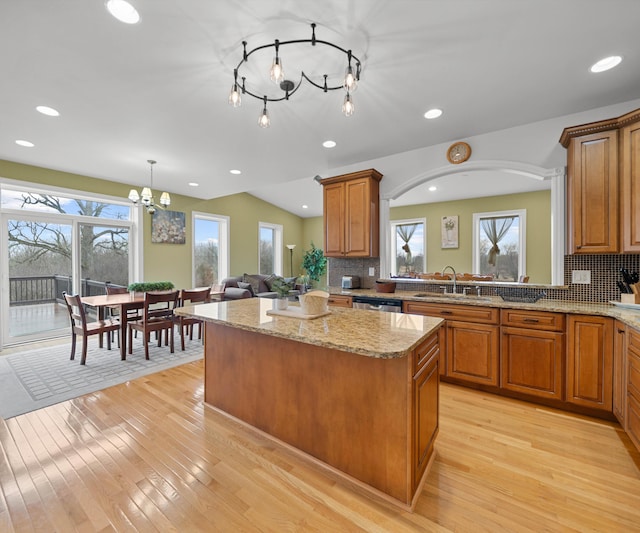 kitchen with brown cabinetry, vaulted ceiling, a center island, and a sink