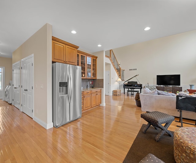 kitchen featuring light wood finished floors, stainless steel fridge with ice dispenser, a sink, decorative backsplash, and glass insert cabinets