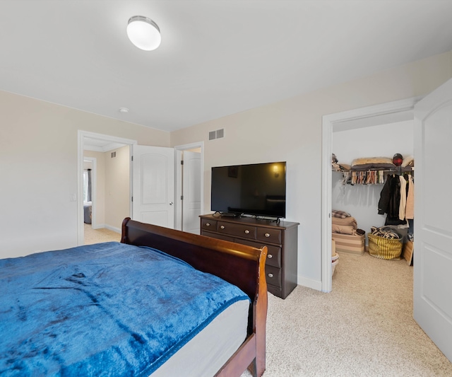 bedroom featuring visible vents, light colored carpet, a walk in closet, and baseboards