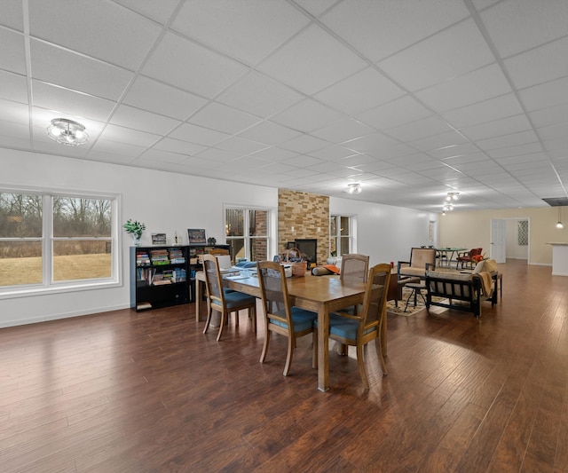 dining room with baseboards, dark wood-style flooring, a drop ceiling, and a large fireplace