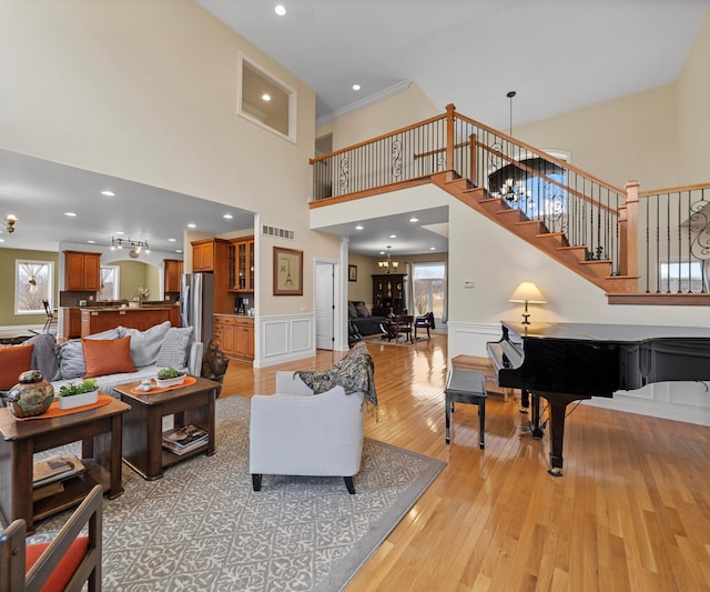 living area with stairs, light wood-style floors, wainscoting, and a chandelier