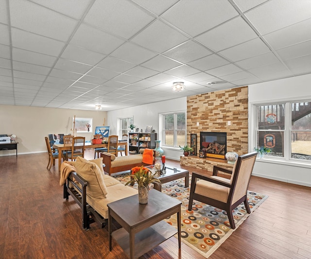 living area with a drop ceiling, a fireplace, and wood finished floors