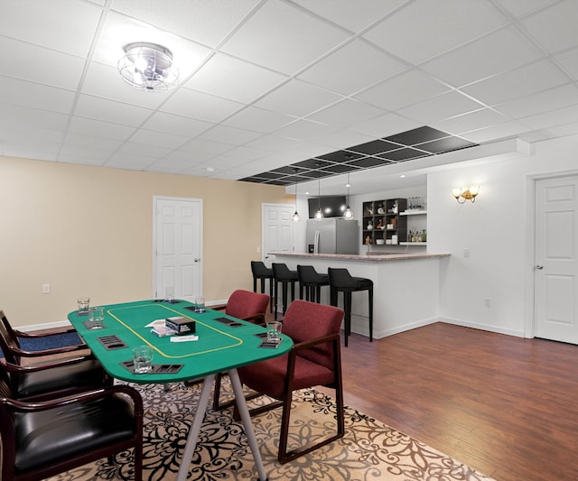 recreation room with a paneled ceiling, dark wood-style flooring, and baseboards