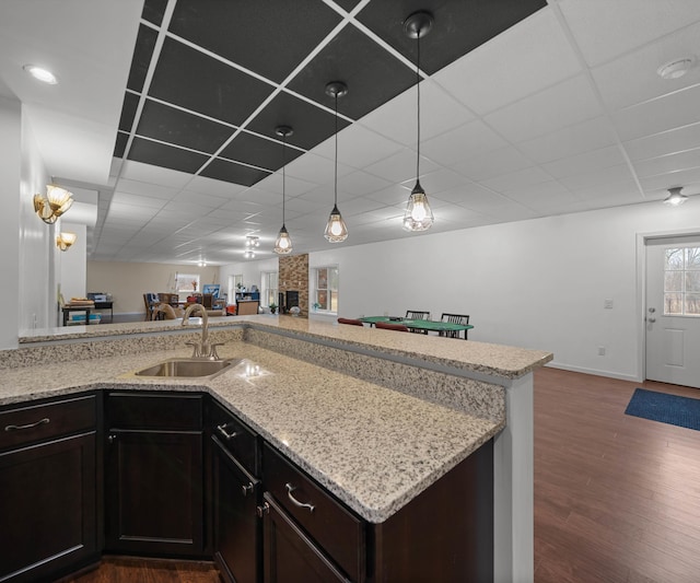 kitchen with open floor plan, light stone counters, wood finished floors, a paneled ceiling, and a sink