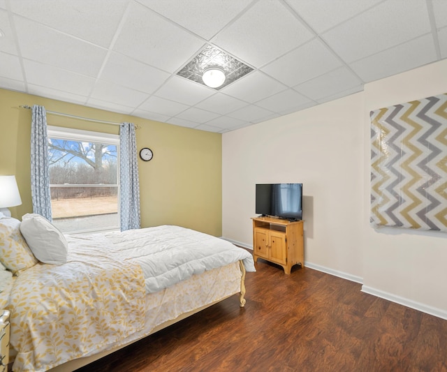 bedroom featuring a drop ceiling, baseboards, and wood finished floors