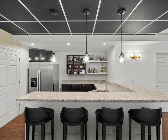 kitchen with a sink, light stone countertops, dark wood-style flooring, and stainless steel refrigerator with ice dispenser