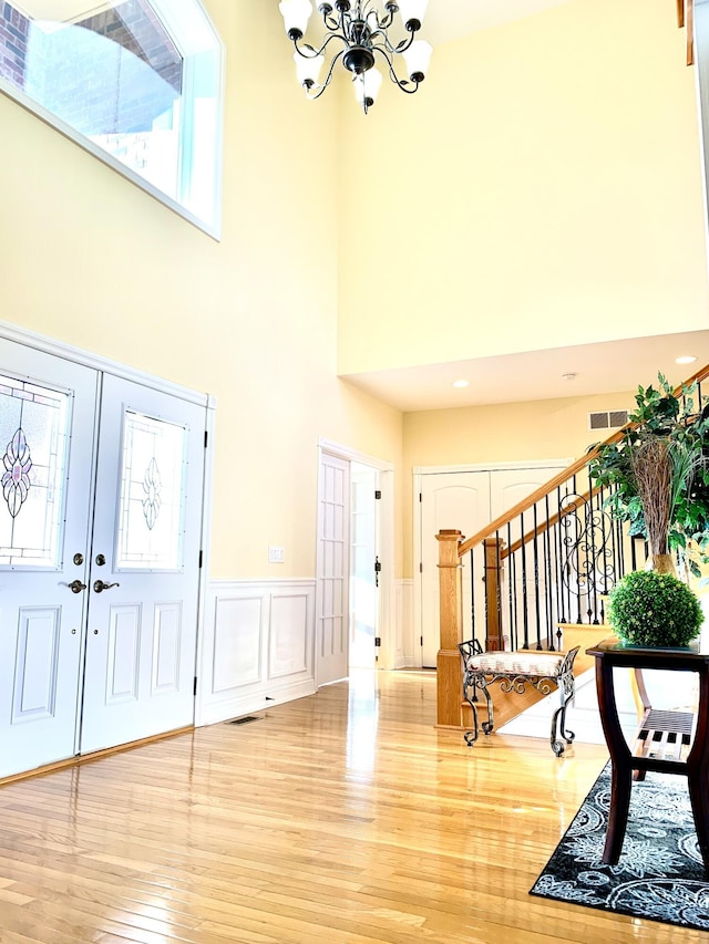 entrance foyer with visible vents, a wainscoted wall, a notable chandelier, light wood-style flooring, and stairs