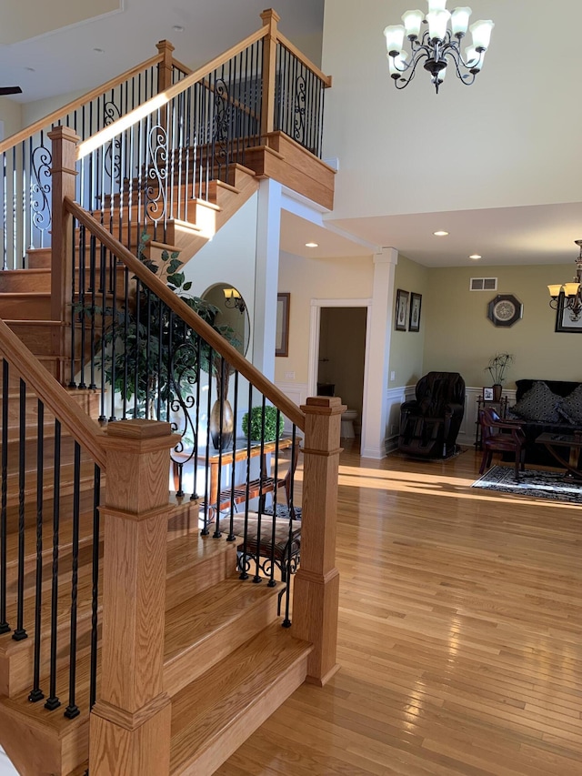 stairs with visible vents, wood finished floors, recessed lighting, a high ceiling, and an inviting chandelier