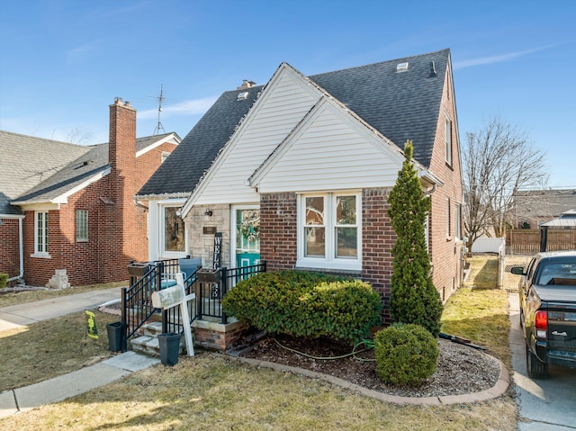 view of front facade with brick siding, roof with shingles, and fence