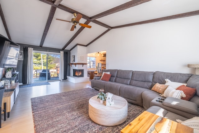 living area featuring vaulted ceiling with beams, a large fireplace, ceiling fan, and wood finished floors