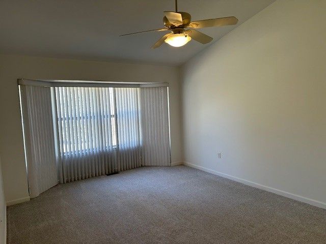 carpeted empty room featuring vaulted ceiling, a ceiling fan, and baseboards