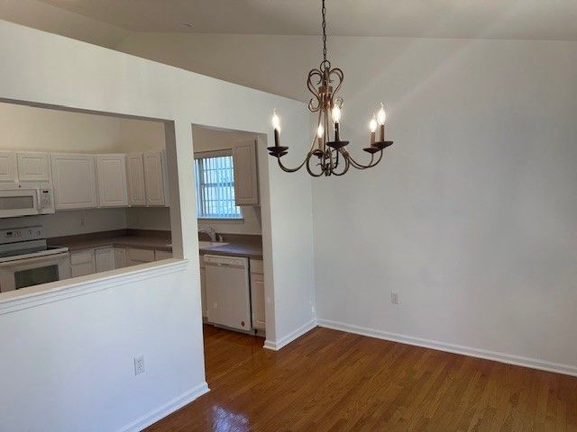 kitchen with white appliances, wood finished floors, baseboards, lofted ceiling, and white cabinetry