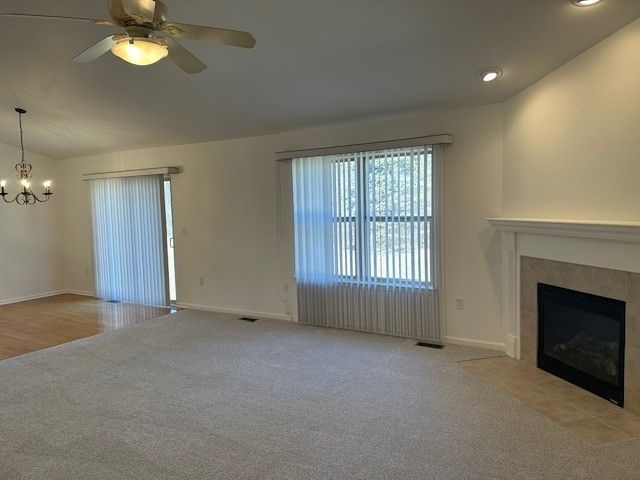 unfurnished living room with carpet flooring, ceiling fan with notable chandelier, baseboards, and a fireplace with flush hearth