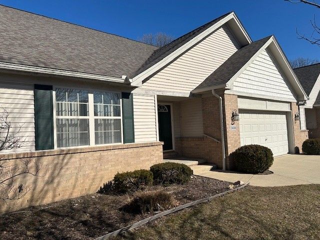 single story home featuring brick siding, an attached garage, concrete driveway, and roof with shingles