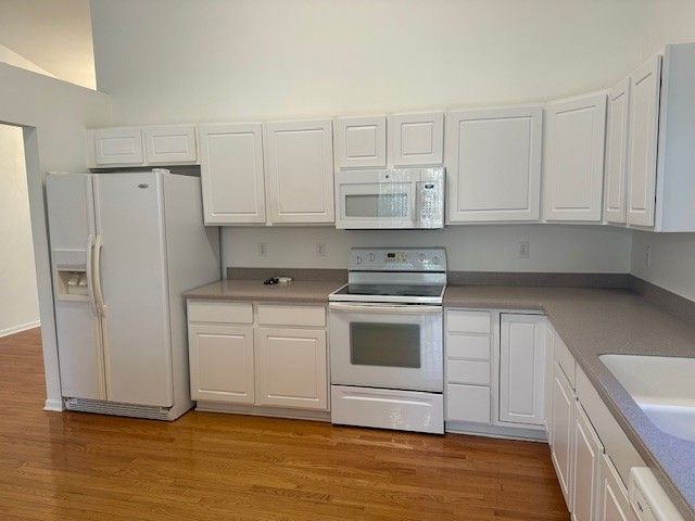 kitchen with white appliances, white cabinets, wood finished floors, and a sink