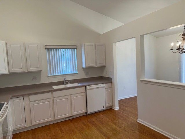 kitchen featuring electric stove, white dishwasher, a notable chandelier, white cabinets, and a sink