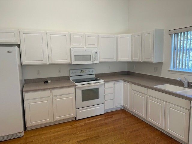 kitchen with white appliances, white cabinets, light wood-type flooring, and a sink