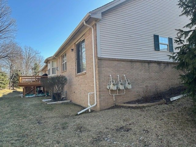 view of side of home with brick siding, a yard, and a deck