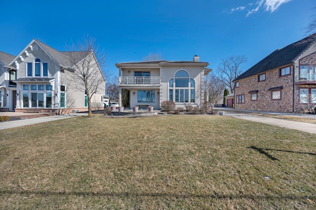 back of property with a yard, a chimney, and a balcony