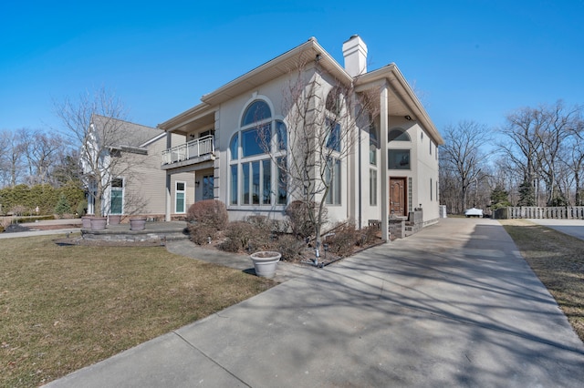 view of property exterior with stucco siding, fence, a yard, a balcony, and a chimney