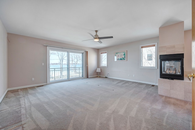 unfurnished living room with a tiled fireplace, baseboards, carpet, and a ceiling fan