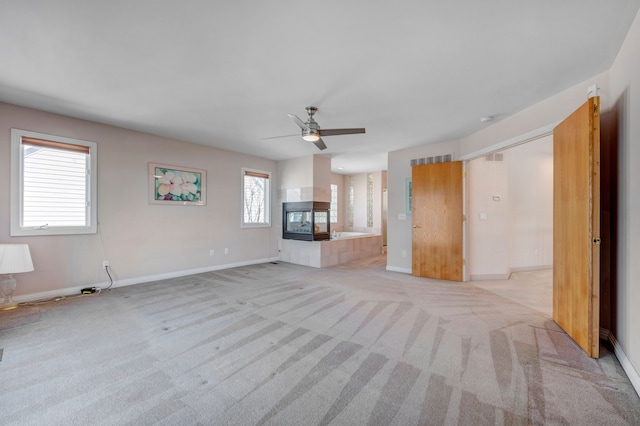 unfurnished living room with baseboards, visible vents, a multi sided fireplace, ceiling fan, and light colored carpet